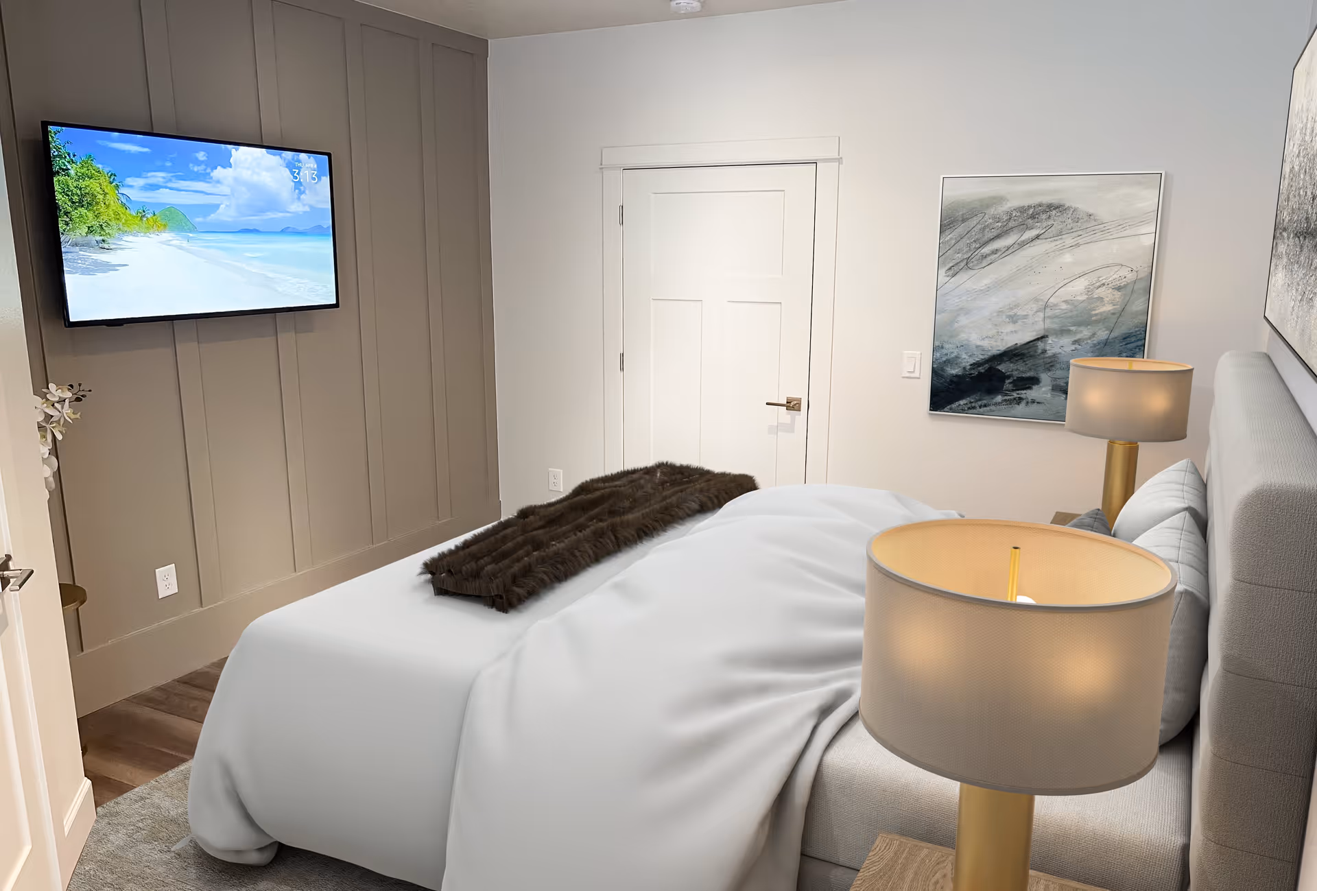 A cozy bedroom with a neatly made bed covered in white bedding and a dark brown throw blanket. Two bedside tables each hold a lamp with a beige shade. A flat-screen TV is mounted on a taupe paneled wall, displaying a beach scene. The room has light-colored walls, a closed white door, and abstract artwork hanging on the wall.