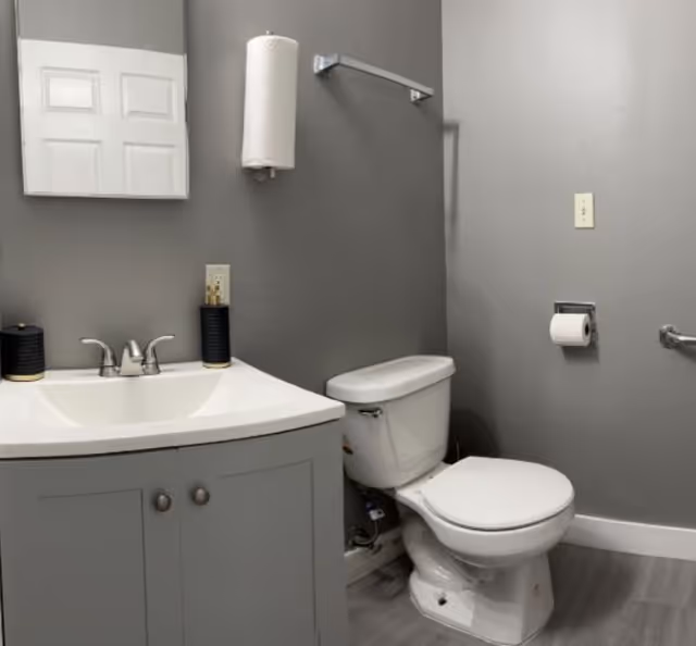 Grey bathroom with sink, mirror, cabinet, and toilet in a senior living facility.