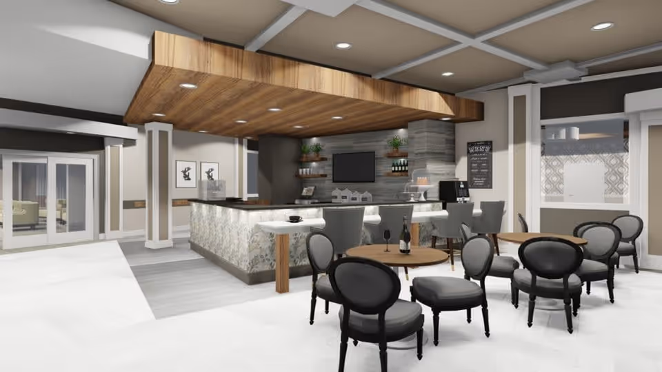 Open communal lounge and café area with a central bar, round tables and upholstered chairs under a wood-accented ceiling.