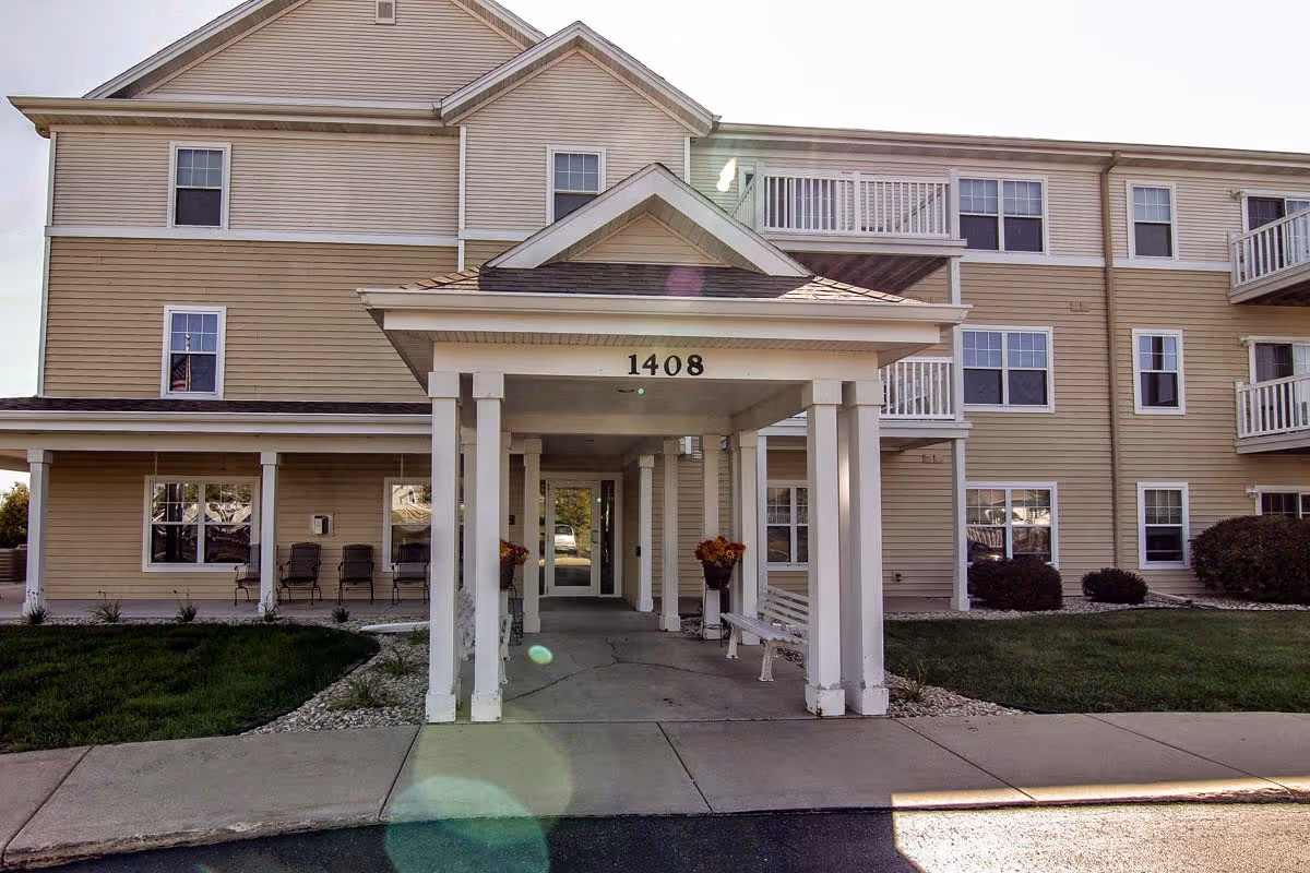Front entrance of a three-story beige senior apartment building with a covered portico numbered 1408.