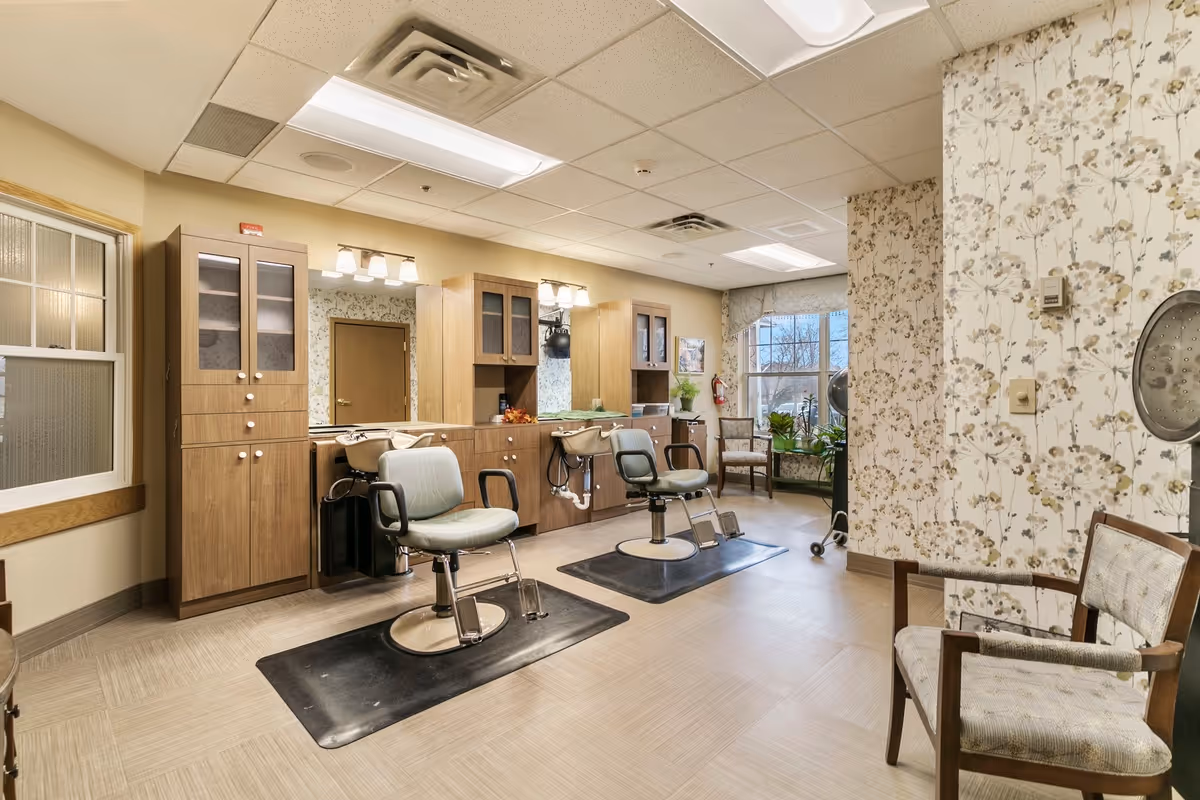 Interior salon area with two barber chairs, mirrors, wooden cabinets, and seating in a bright room.