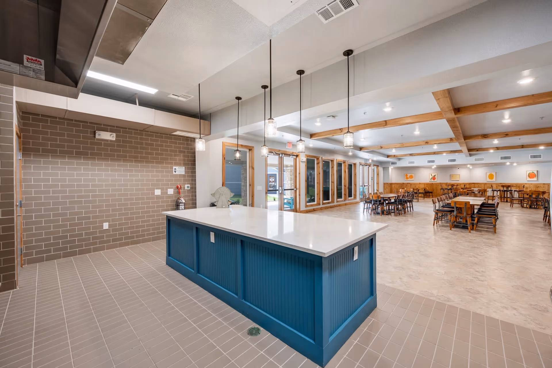 Spacious communal dining area with a central blue island, pendant lights, and multiple tables and chairs.