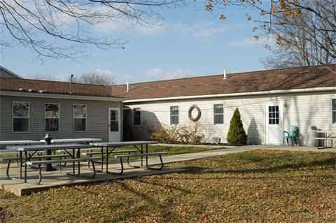 Single-story assisted living facility exterior with a picnic table, fallen leaves, and a wreath.