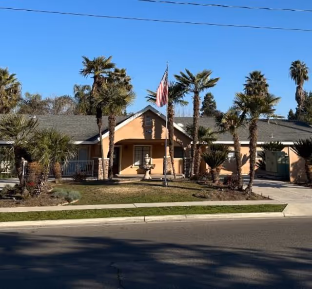Front view of a tan senior living facility with palm trees and an American flag.