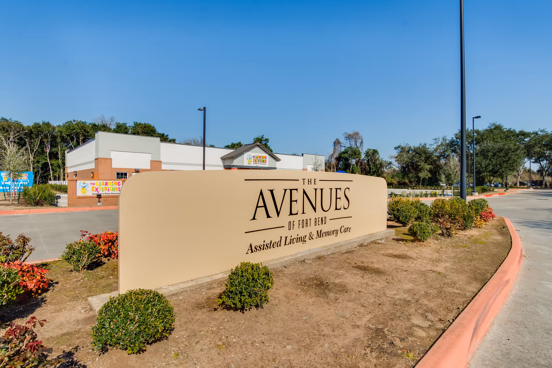 A sign for The Avenues of Fort Bend assisted living and memory care, surrounded by landscaped bushes.