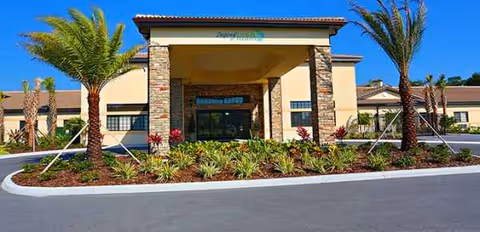 Exterior view of Inspired Living Sarasota entrance with palm trees and landscaped beds
