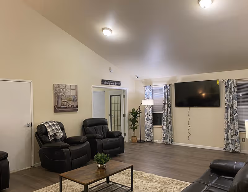 Bright living room with leather recliners, a wooden coffee table, wall-mounted TV, and patterned curtains.