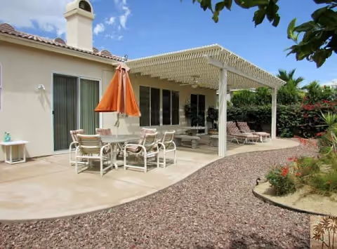 Backyard patio with a covered pergola, an outdoor dining table with an orange umbrella, lounge chairs, and gravel landscaping.