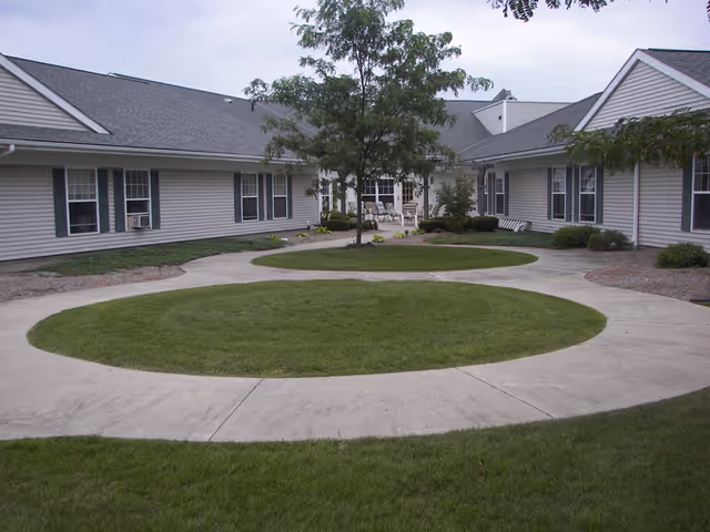 A landscaped courtyard with circular grass islands and a concrete walkway surrounded by single-story vinyl-sided senior living buildings.