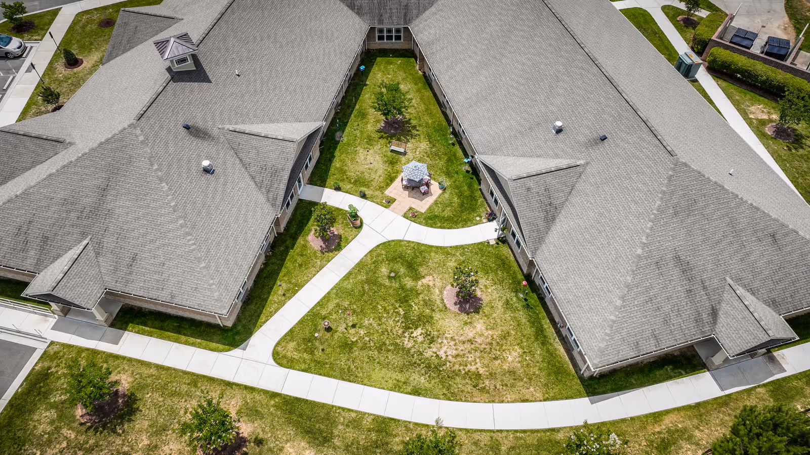 Aerial view of two connected buildings surrounding a grassy central courtyard with paved walkways and a small seating area.