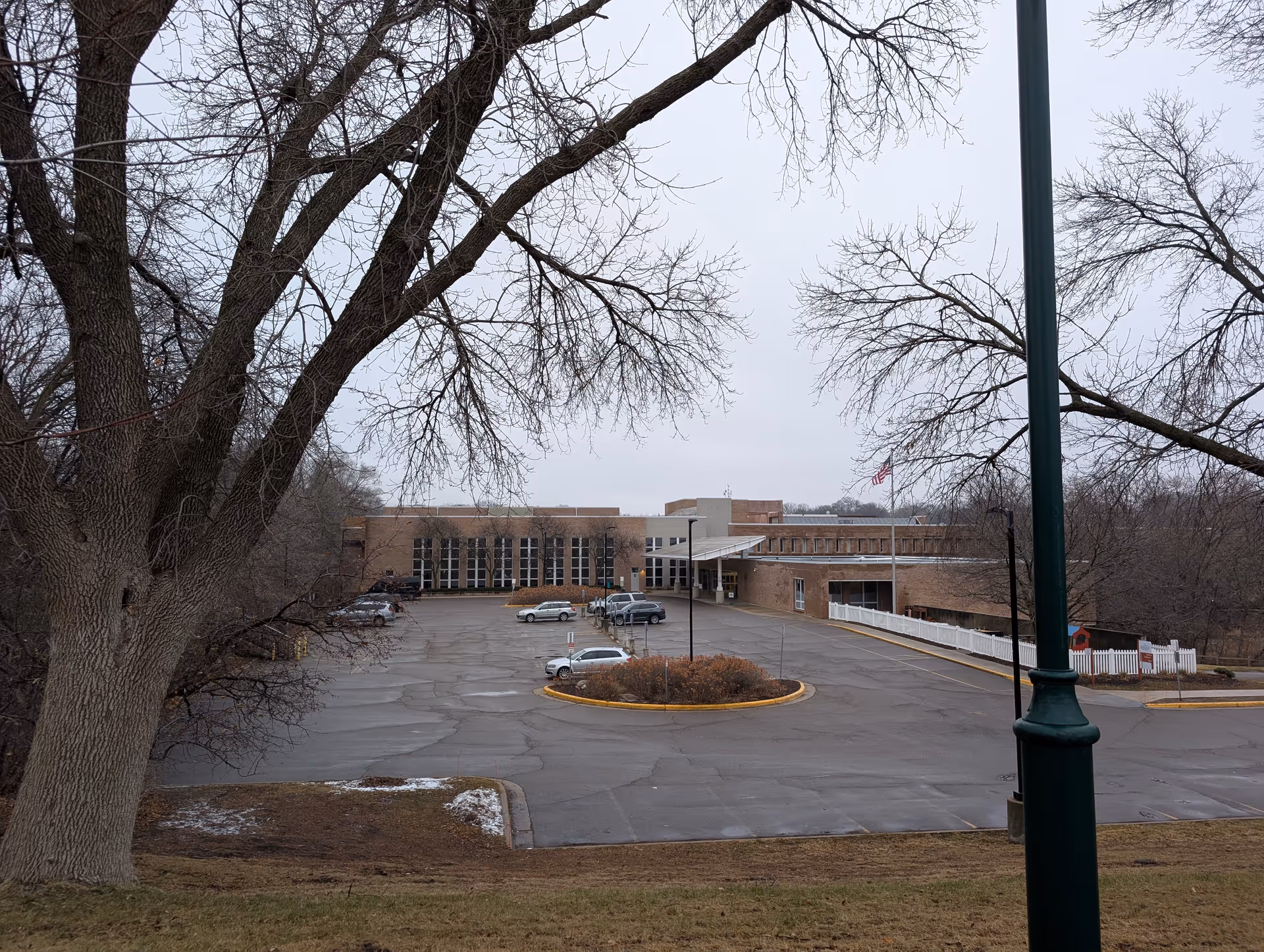 Exterior view of Courage Kenny Rehabilitation Institutes building with a parking lot in front, several parked cars, leafless trees, and an overcast sky.