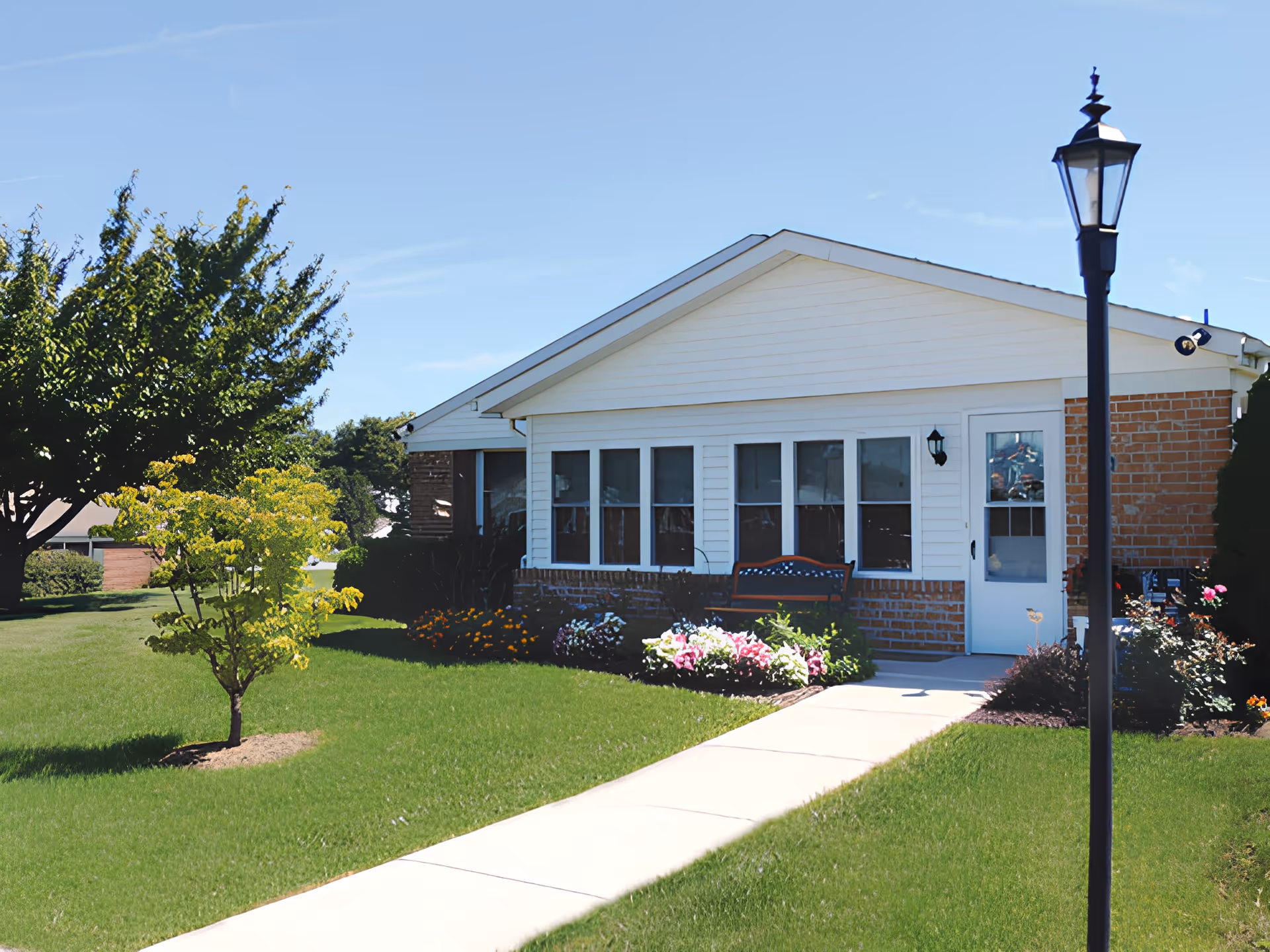 Single-story brick and siding building front with a walkway, lawn, flower beds, bench, and lamppost.