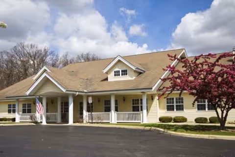 Exterior view of Cedar Creek of Muncie facility with porch, flag, and pink flowering tree.