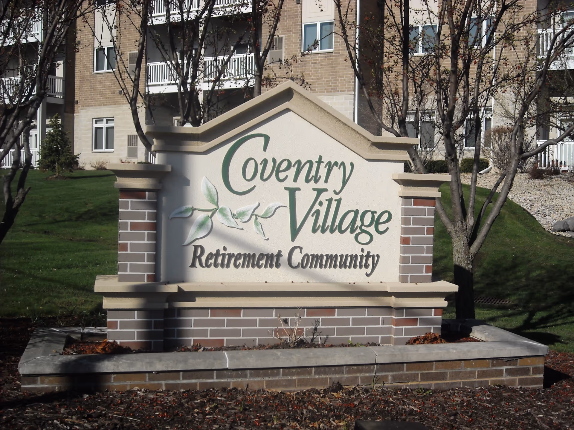 Stone and brick sign for Coventry Village Retirement Community with trees and a building in the background.