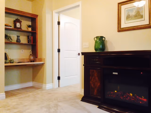 Interior living area featuring an electric fireplace, a built-in shelving desk, and an open white door.