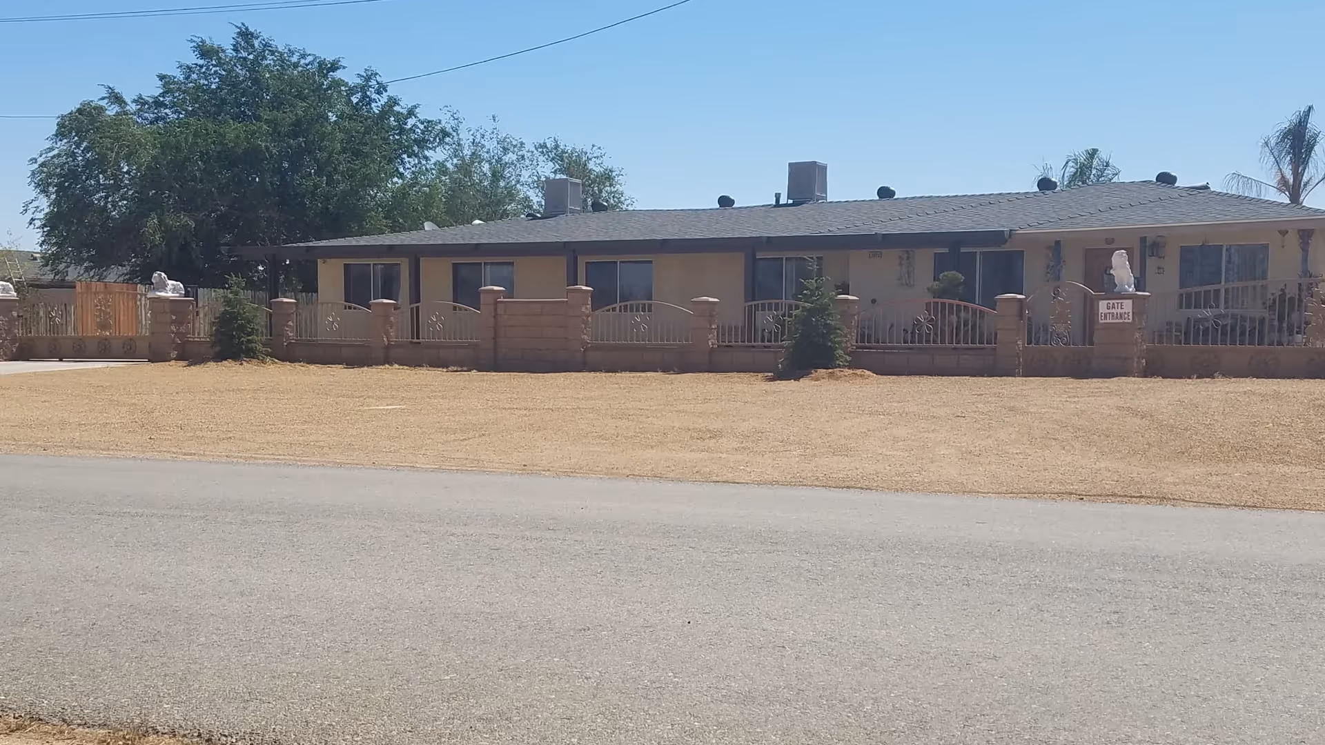 Single-story residential building with a low decorative fence and a dry front yard under a clear blue sky.
