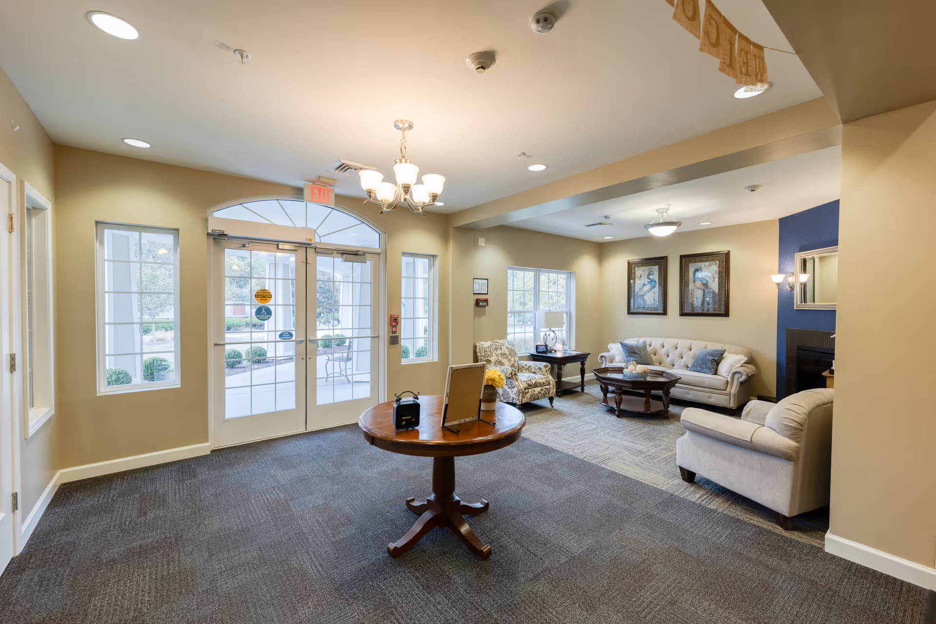 Bright entry lobby with a round table and a seating area of sofas and armchairs near glass double doors.
