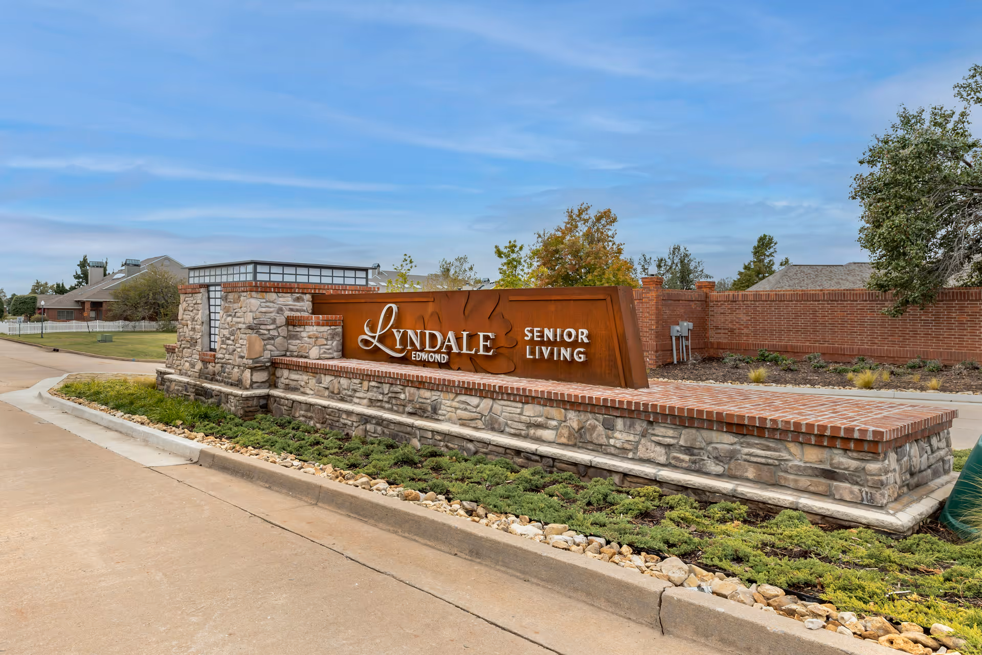 Stone and brick entrance sign for Lyndale Edmond Senior Living with landscaping and a clear sky in the background.