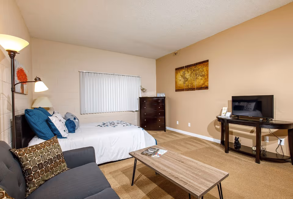 Senior apartment bedroom with bed, sofa, coffee table, dresser, and wall-mounted TV.