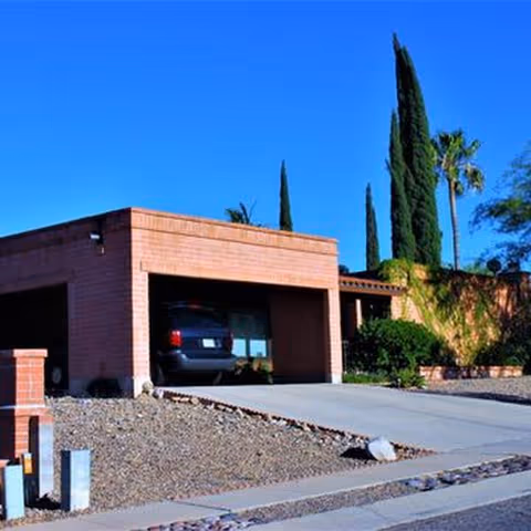 Single-story brick facility exterior with a driveway, car in a garage, and desert landscaping.
