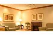 Comfortable sitting room with two upholstered sofas, a coffee table, lamps, framed artwork, a small fireplace, and a potted plant.