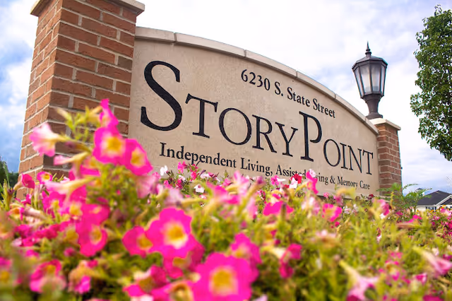 Entry sign reading "StoryPoint" with address and service text, surrounded by pink flowers and a lamp post.