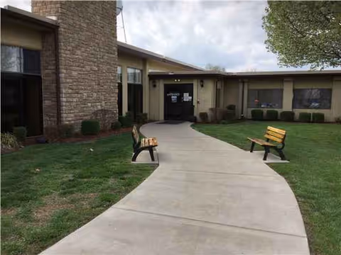 Curved walkway to the entrance of a senior living facility with two benches.