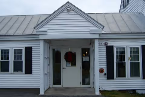 White, single-story building entrance with double doors and a wreath on the porch.