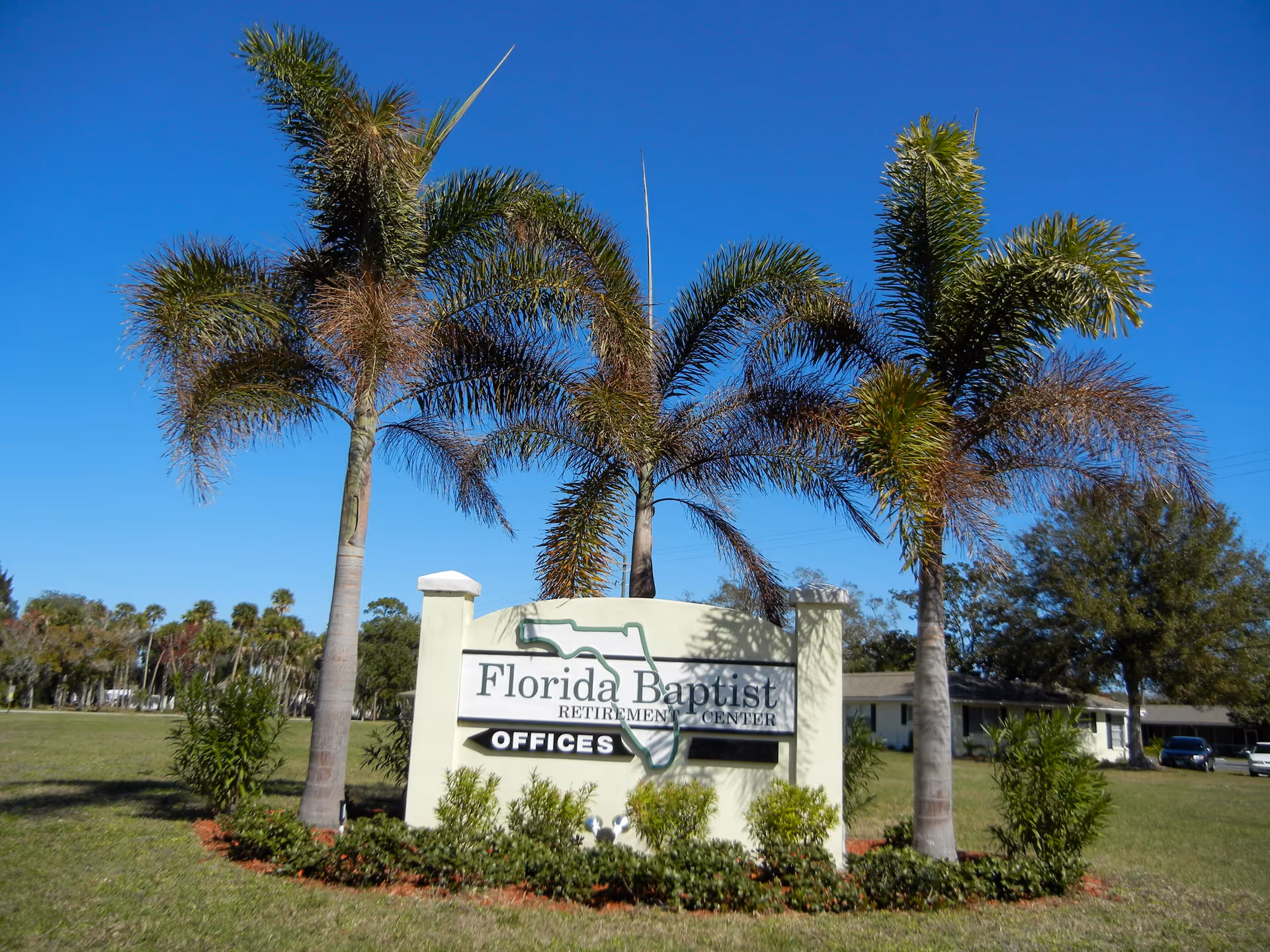 Outdoor view of the Florida Baptist Retirement Center sign surrounded by palm trees and greenery under a clear blue sky.
