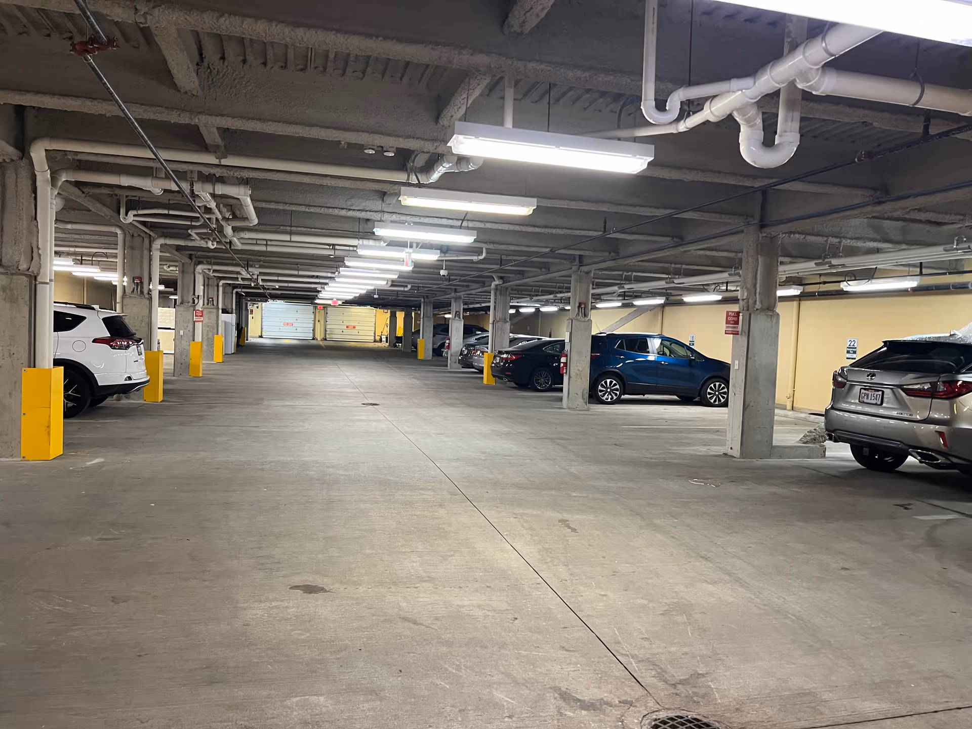 Indoor parking garage with several parked cars along the sides, concrete pillars, and overhead fluorescent lighting.