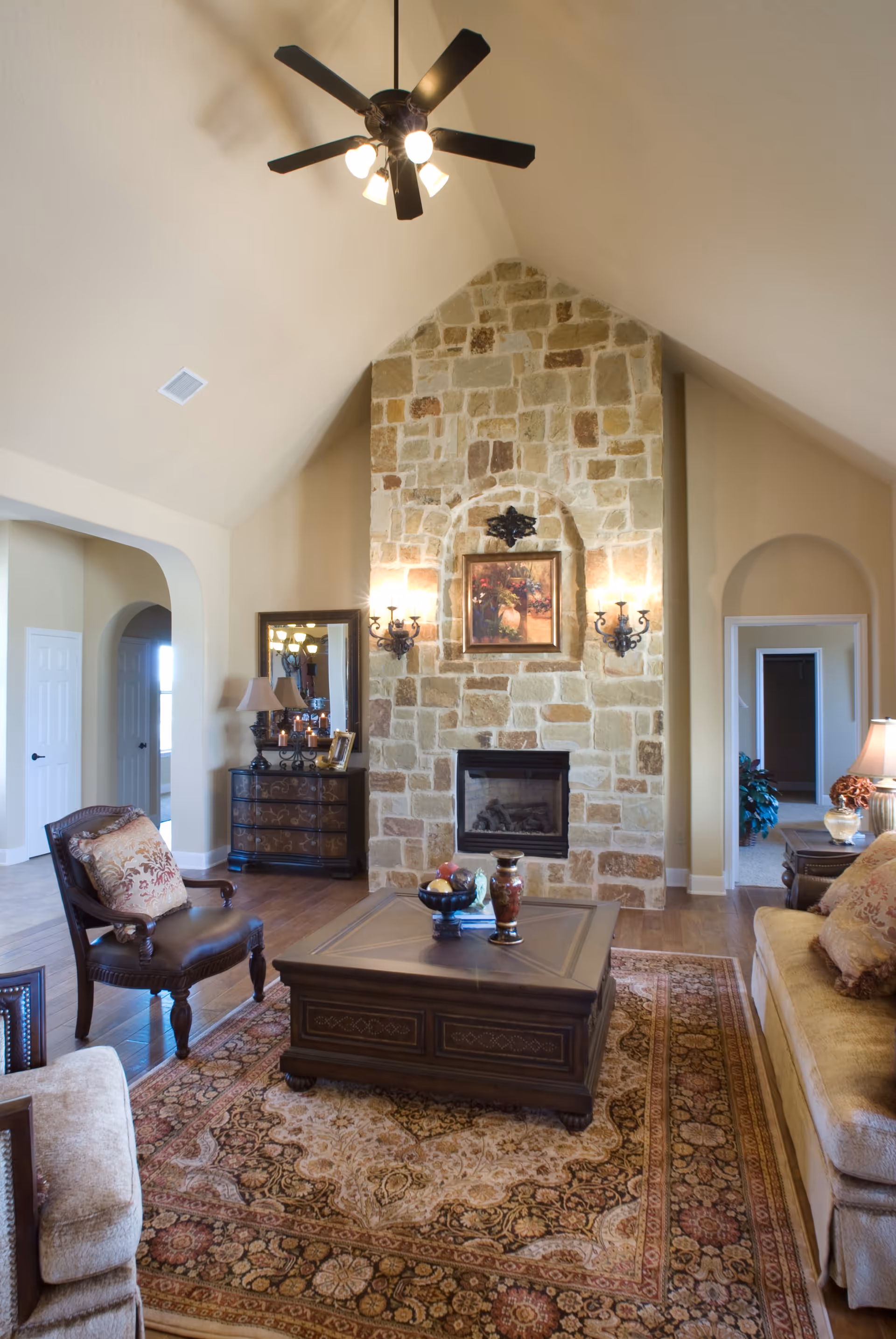 Spacious living room with a vaulted ceiling and stone fireplace, furnished with a coffee table, upholstered sofas and chairs on a patterned area rug.