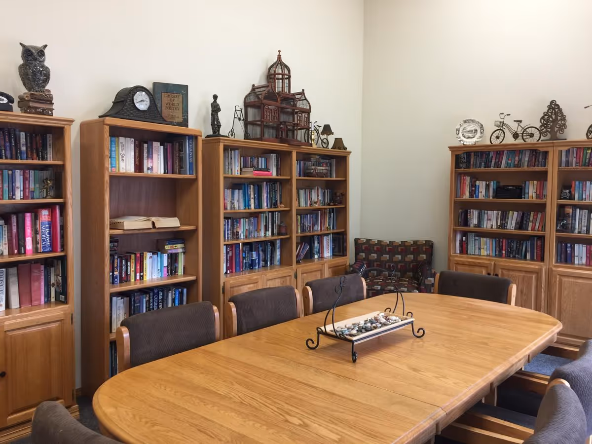 Long wooden table with chairs in a library-style room lined with bookshelves and decorative accents.