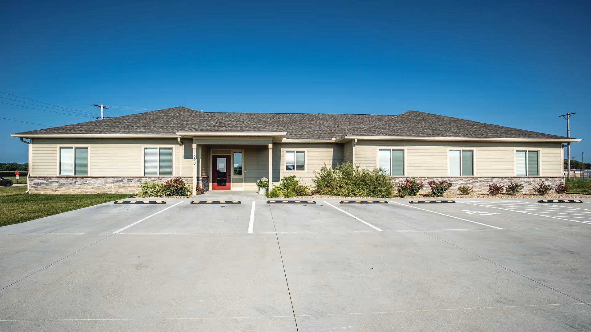 Single-story beige building with a central entrance and empty parking spaces under a clear blue sky.