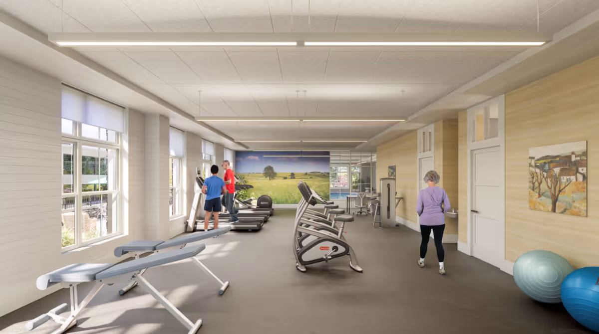 A spacious fitness room in a senior living facility with exercise equipment including treadmills, stationary bikes, and weight benches. Two people are using the treadmills, and another person is standing near the wall with exercise balls. Large windows on the left side let in natural light, and a mural of a green field with a tree is visible on the far wall.