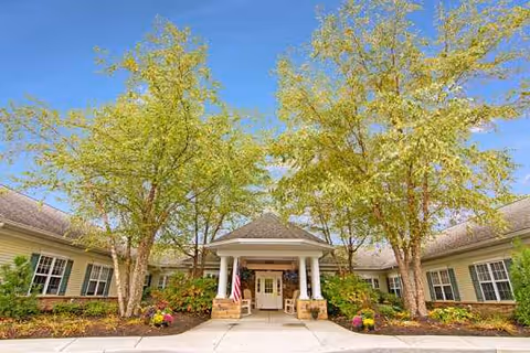 Senior living facility front entrance with columns, walkway, and landscaped trees.