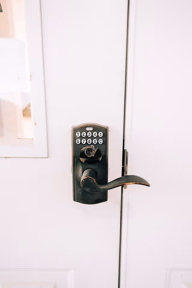 Close-up of a black keypad door lock with a lever handle mounted on a white door with a small window on the left side.