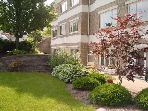 Exterior view of a brick senior living building with lawn and patio seating.