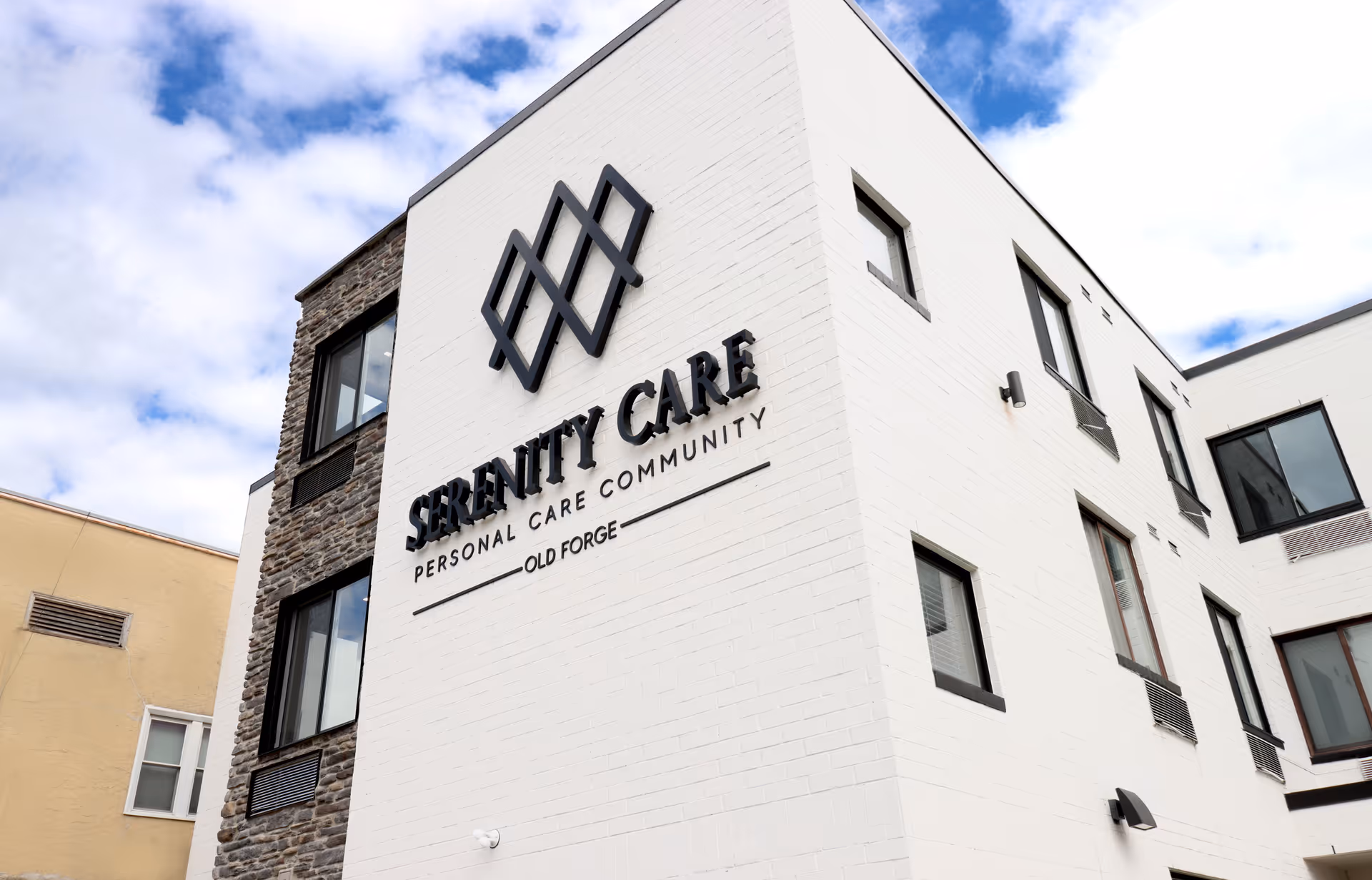 White multi-story building exterior with 'Serenity Care Personal Care Community Old Forge' signage and a decorative logo.
