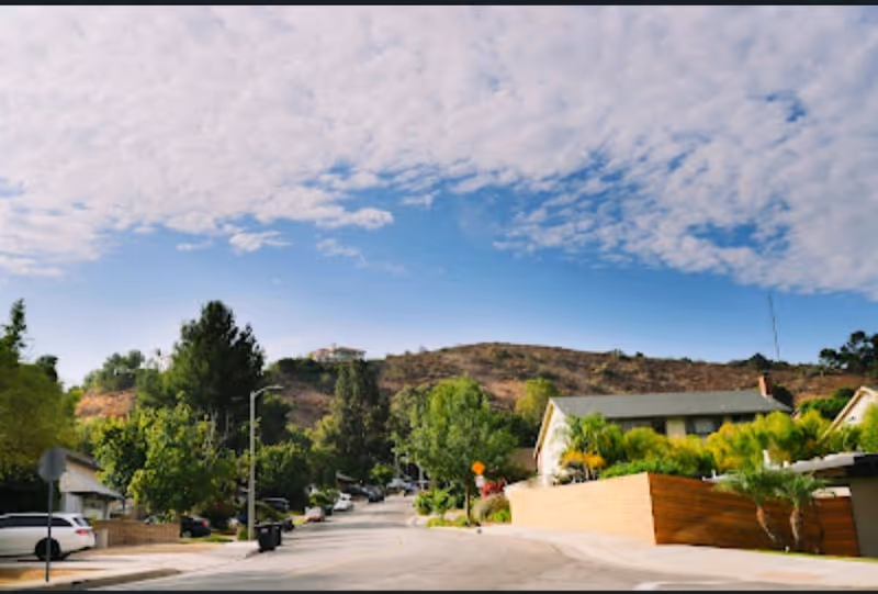 Outdoor street view of a senior living campus with trees, houses, and hills.