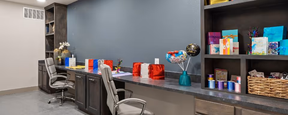 Long counter workspace with swivel chairs, built-in shelving and cabinets, and gift-wrapped packages and craft supplies against a blue-gray wall.