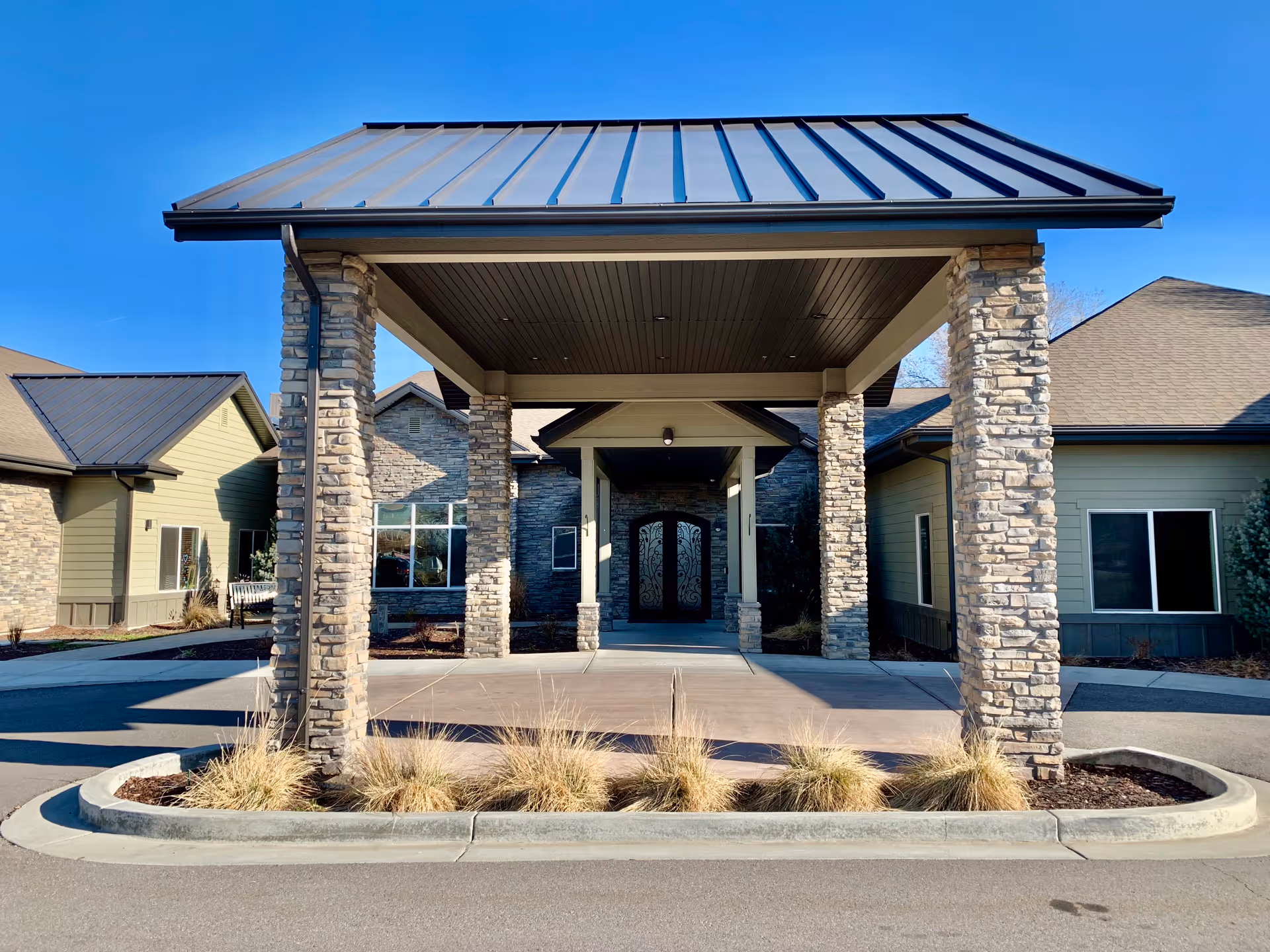 Main covered entrance with stone pillars and a metal roof at the front of a one-story building.