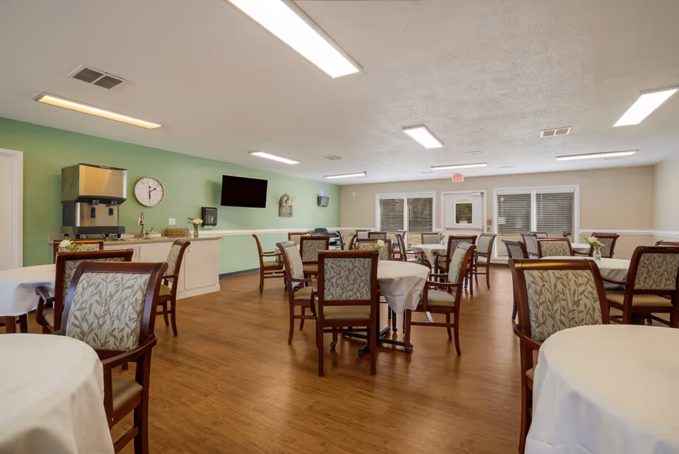 Senior living dining hall with round tables, cushioned chairs, and a service counter.