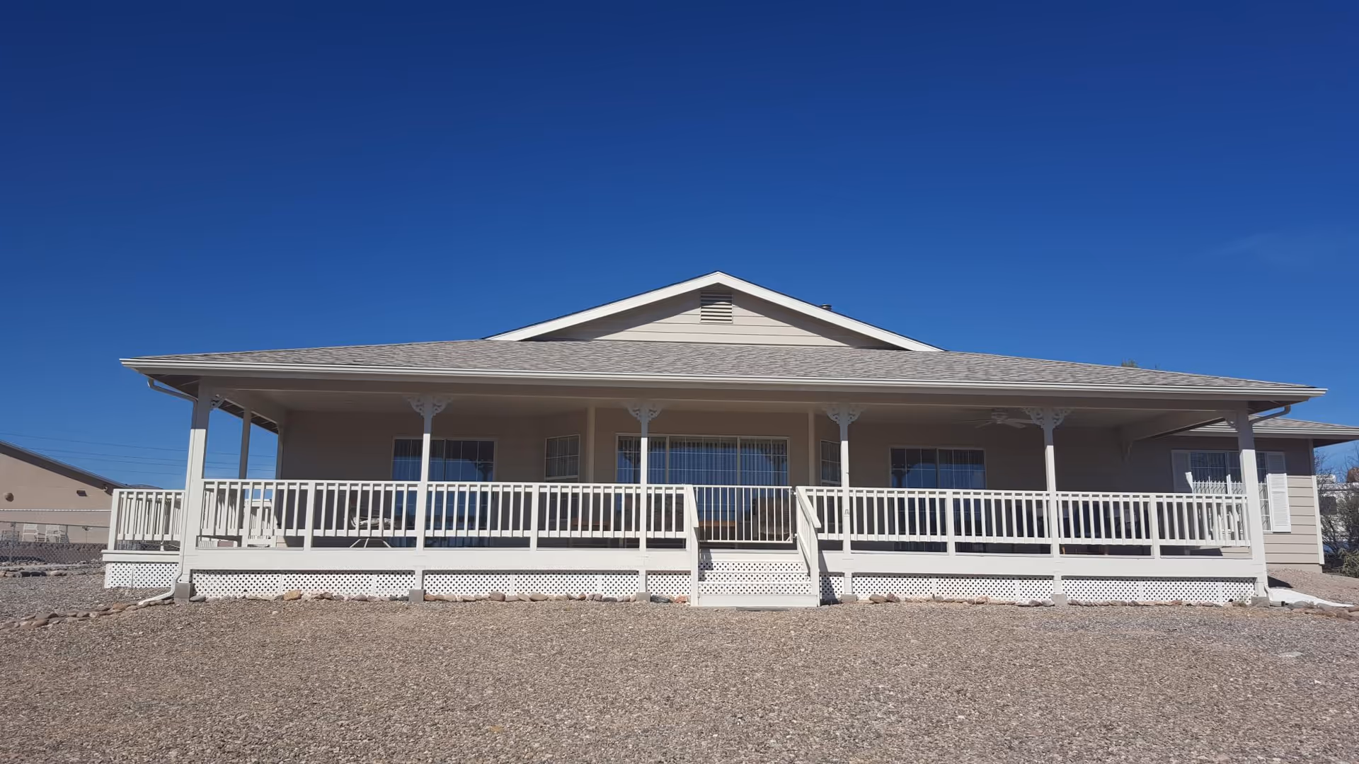 Single-story building with a wide covered porch and white railing under a clear blue sky.