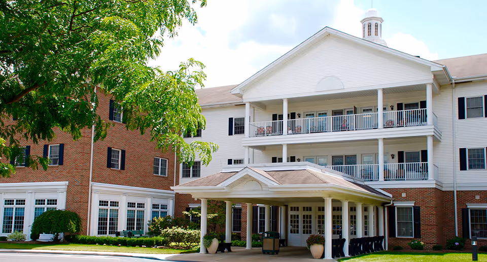 Front exterior of a multi-story senior living facility with a covered entrance, balconies, and landscaped grounds.