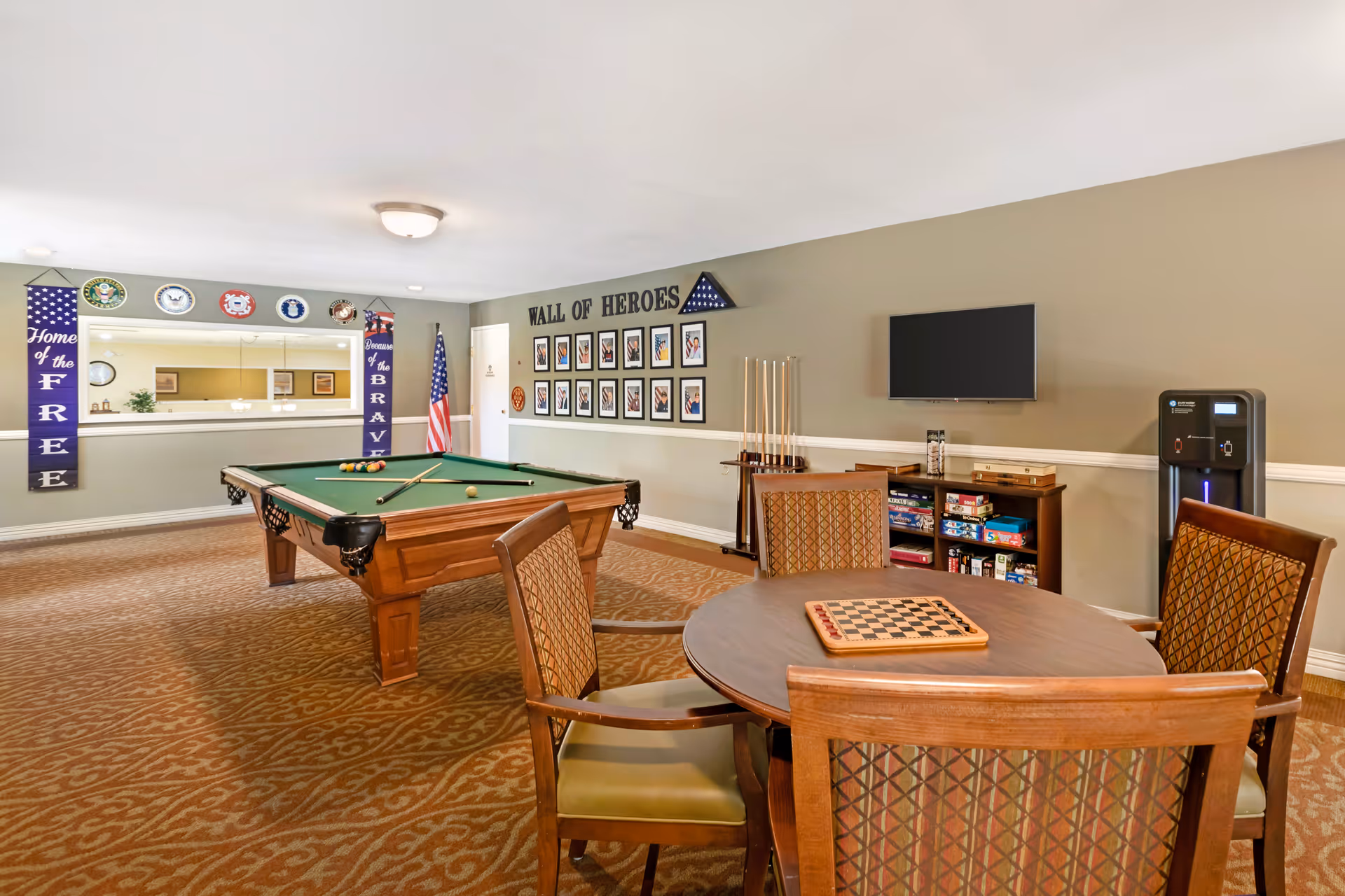 Recreation room with a pool table, round game table and chairs, TV, and a 'Wall of Heroes' display.
