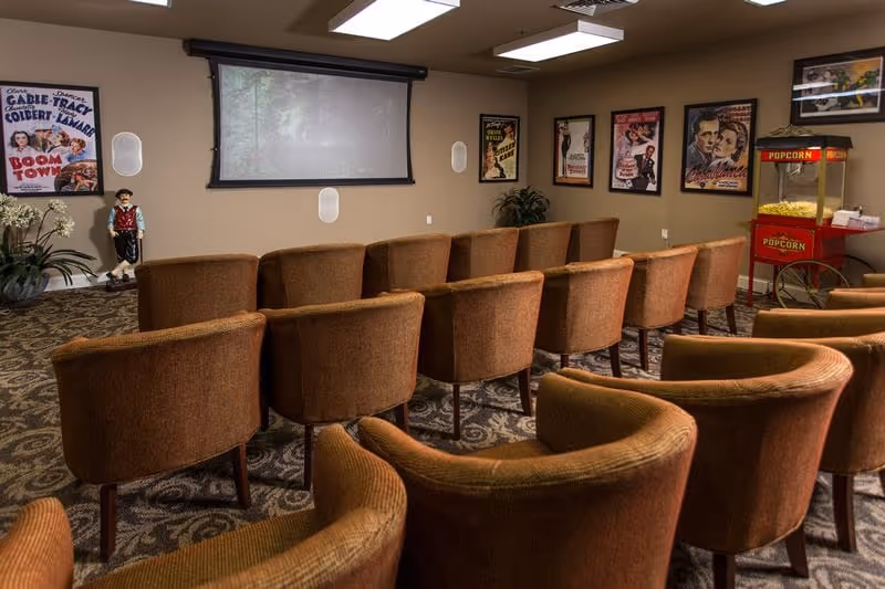 Small screening room with rows of brown upholstered chairs facing a pull-down projection screen, movie posters on the walls and a popcorn machine.