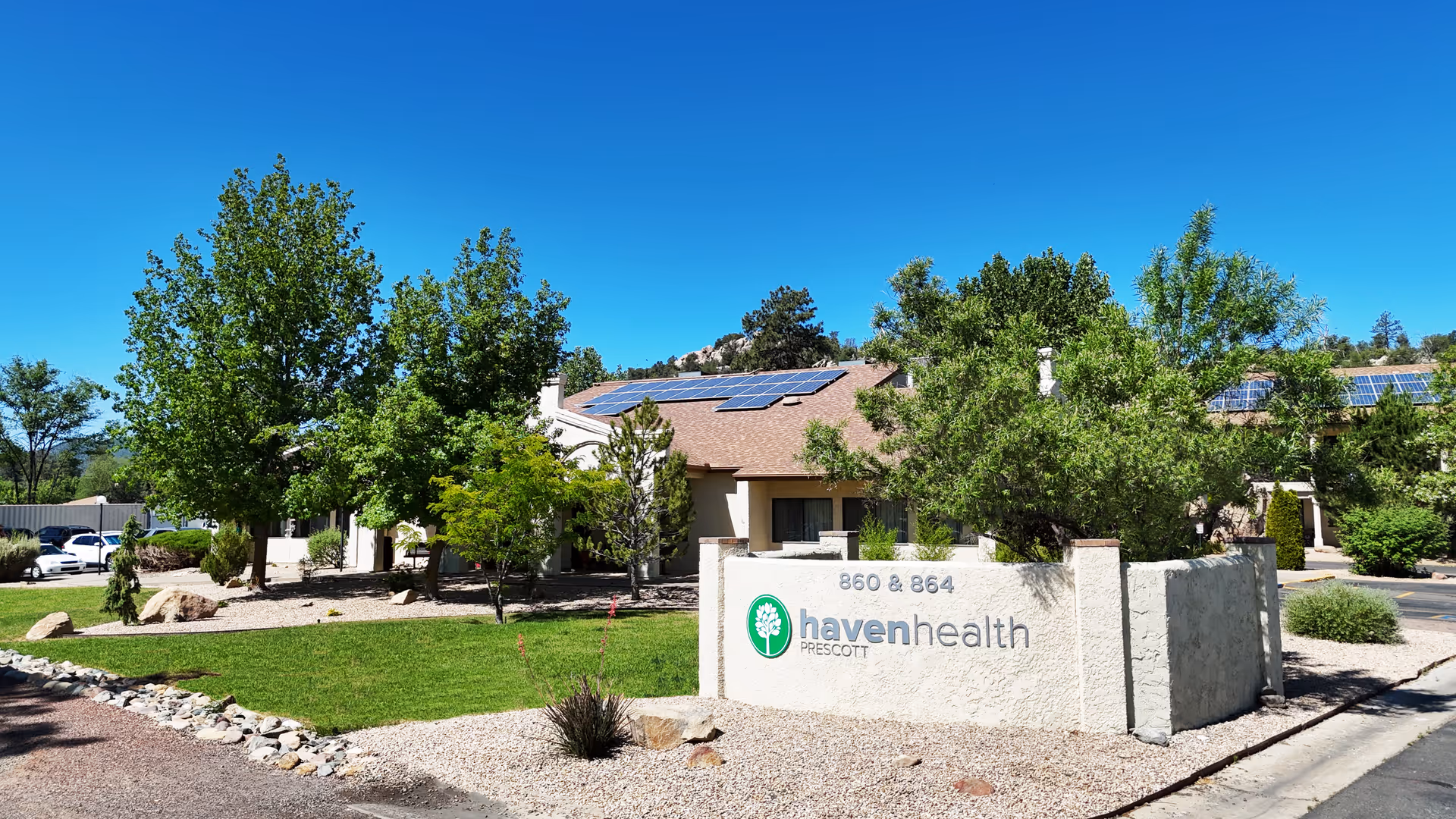 Stone entrance sign reading 'havenhealth Prescott' in front of a one-story building with trees, lawn, and solar panels under a clear blue sky.