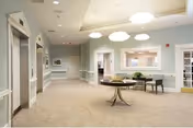 Bright senior living facility lobby with arched openings, a round table, and seating area.