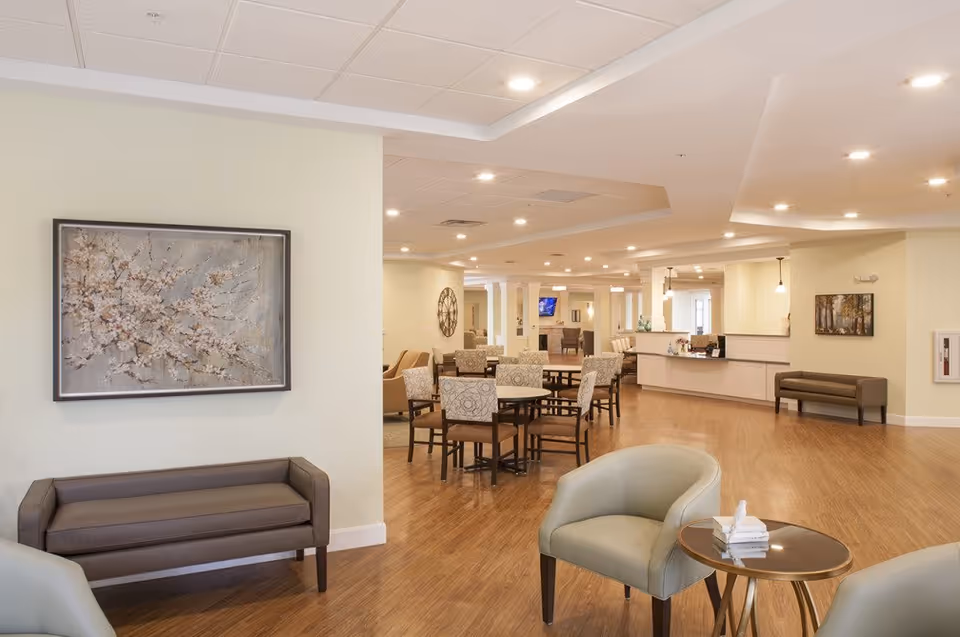Bright open common area with multiple dining tables, lounge chairs, and a reception desk.
