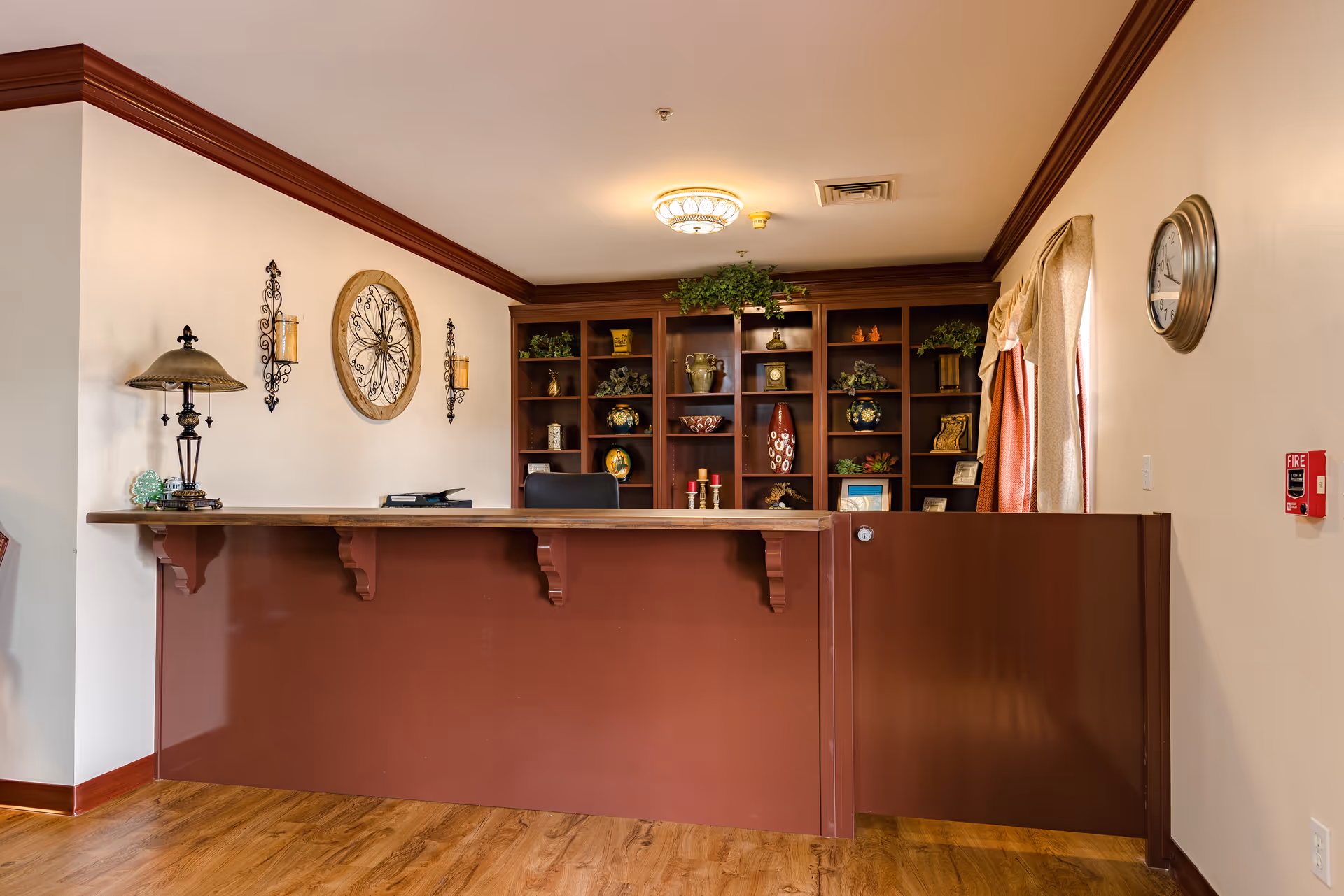 A front reception desk with shelving, decorative items, and lamps in a warmly decorated retirement community lobby.